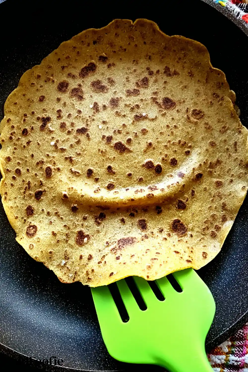 Cooking Chickpea Tortilla in Nonstick Skillet Chickpea tortilla cooking in nonstick pan with green spatula
