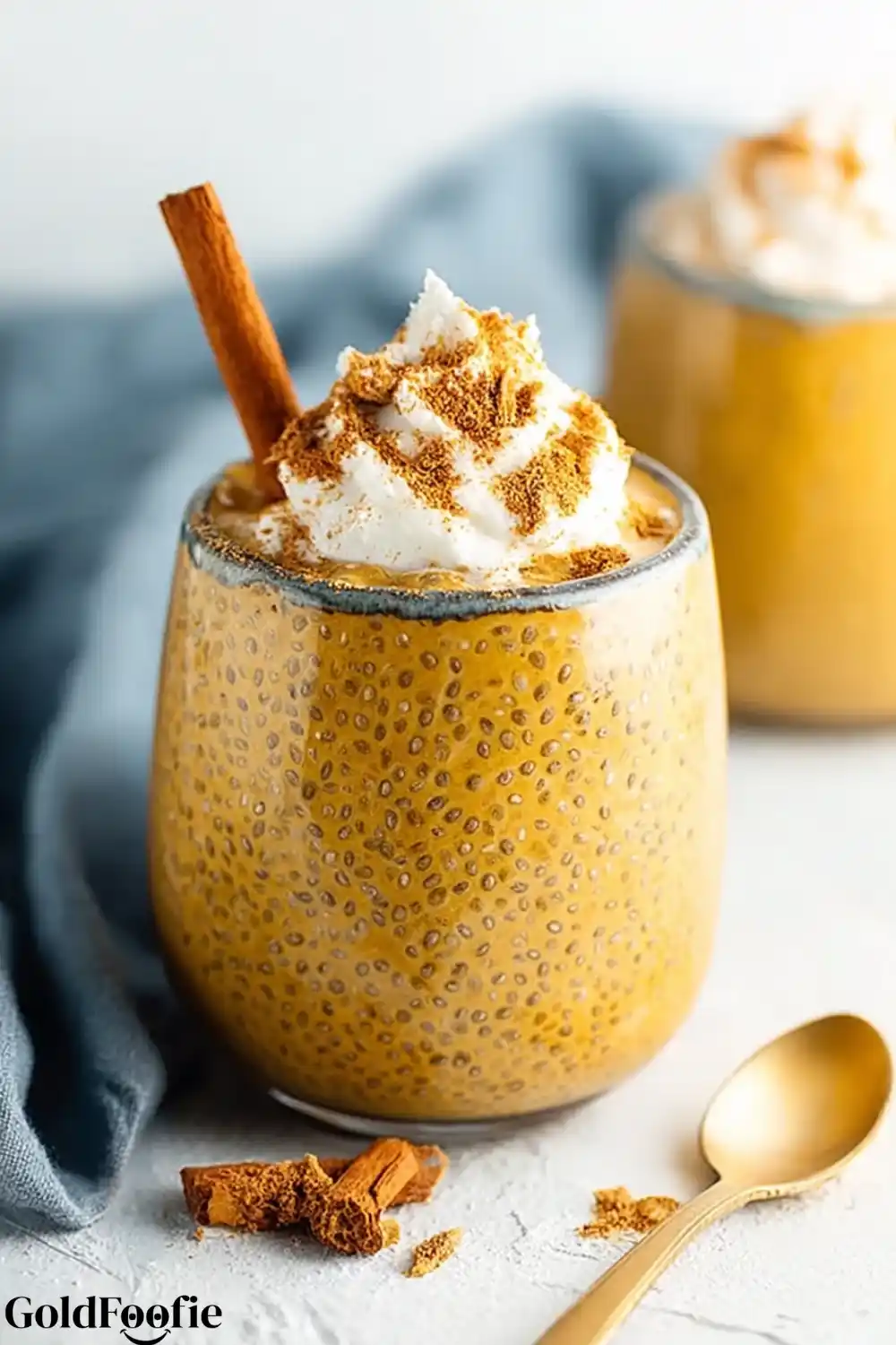 High-Protein Pumpkin Chia Pudding 5 Pumpkin chia pudding topped with cream and cinnamon, served with gold spoon.