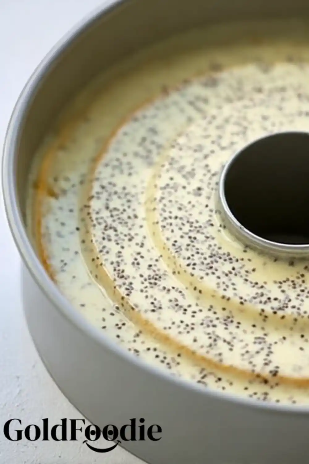 Cake Batter Prep Unbaked orange chia cake batter sprinkled with chia seeds in a tube pan.