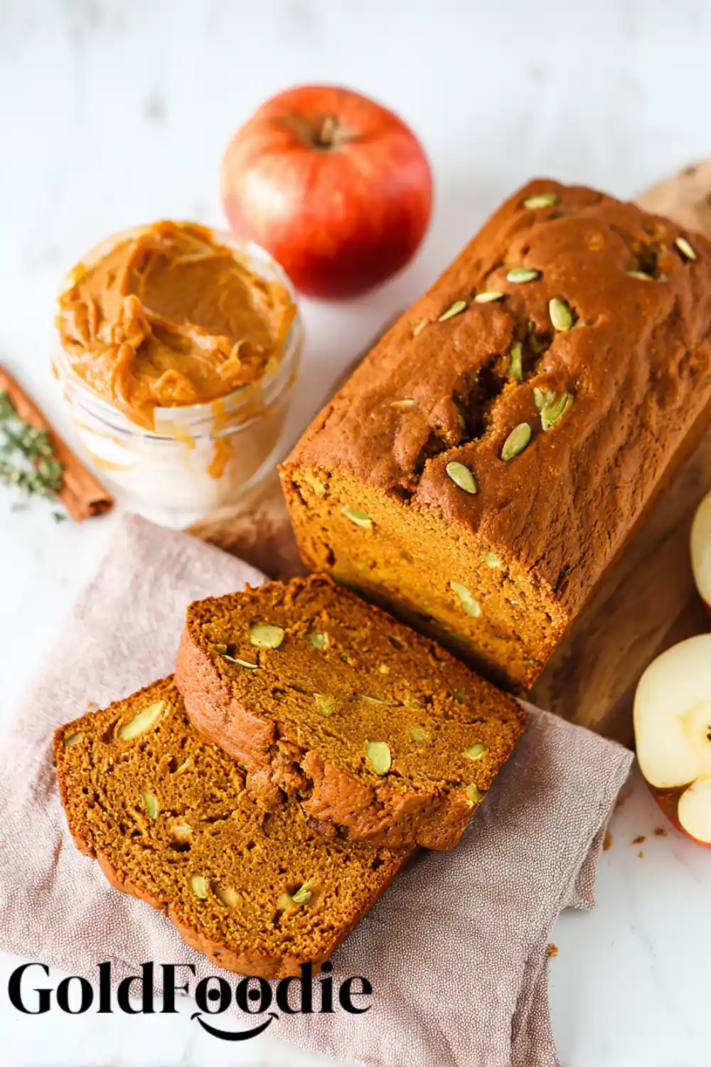 Easy Pumpkin Apple Bread Two slices of pumpkin apple bread leaning against the loaf, with pumpkin seeds and fresh apple slices.